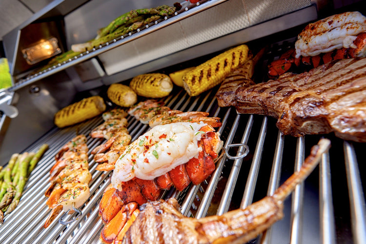 Lobster tails, steaks, shrimp skewers, corn and asparagus on the stainless steel grates of a Bull grill
