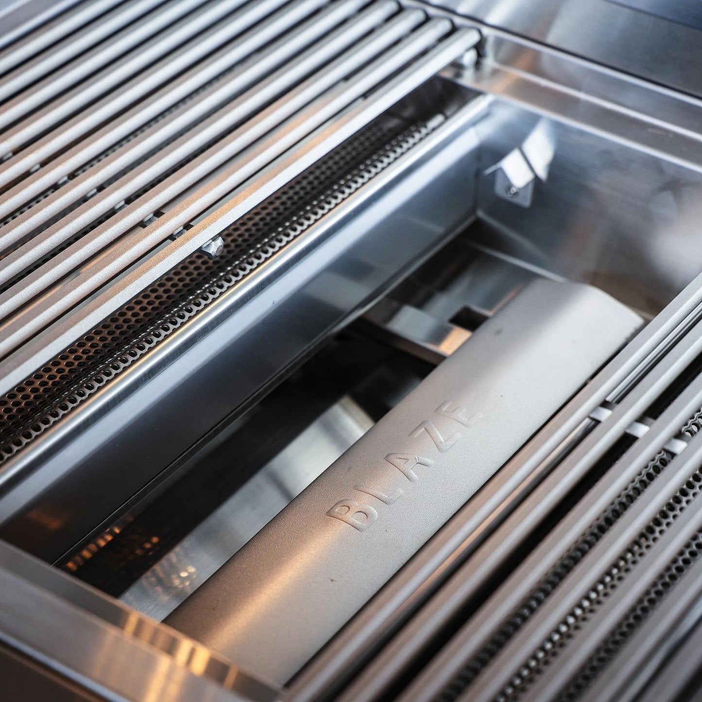 Stainless steel flame-tamer system beneath the cooking grates