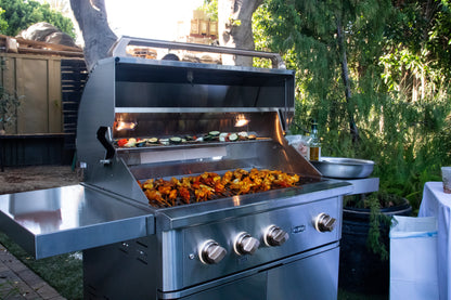 Wildfire Ranch Pro grill on a stainless steel Wildfire grill cart, cooking vegetables and kebabs outdoors